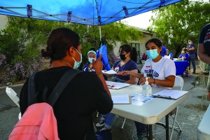 people in masks sit at folding table outdoors